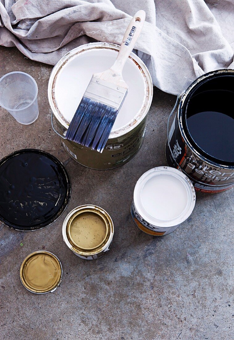 Open tins of various paints with paintbrush and cloth