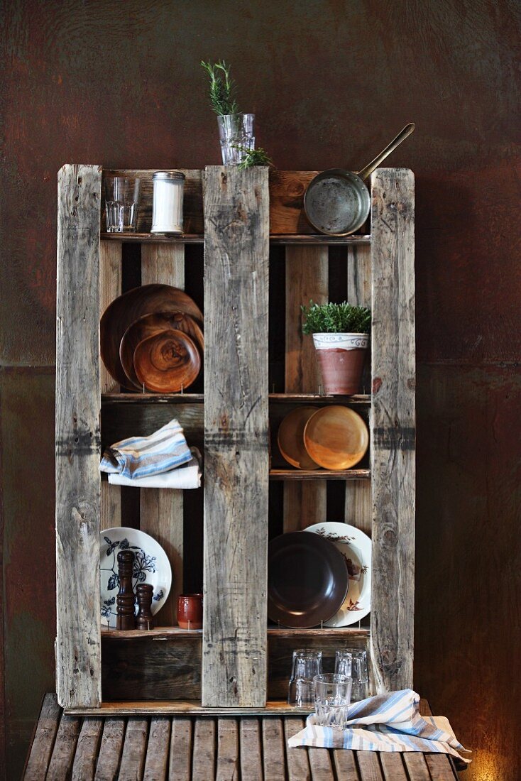 Decorative plates on wooden pallet used as open shelving against corten steel wall