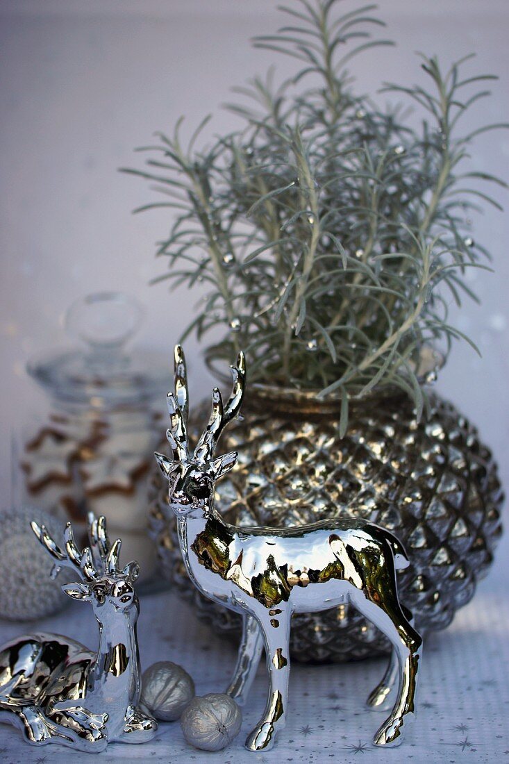 Silberne Hirschfiguren vor einem Rosmarinstrauch in einer Vase