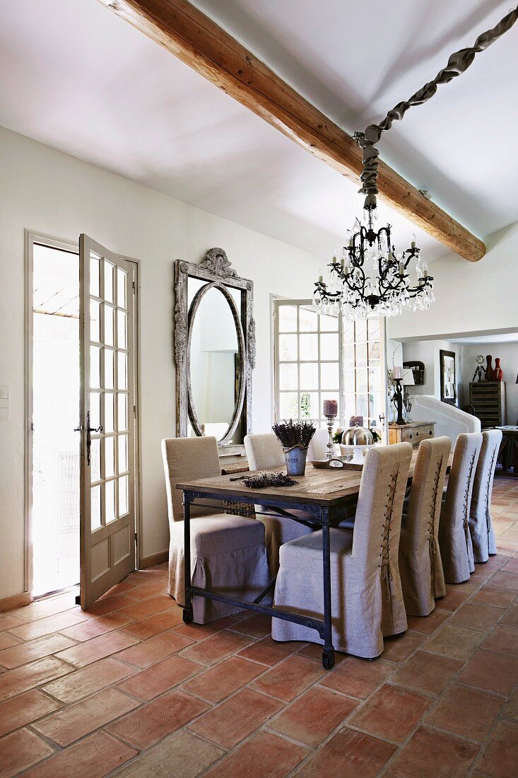 Chairs with loose covers at dining table next to open terrace doors in renovated country house with terracotta floor