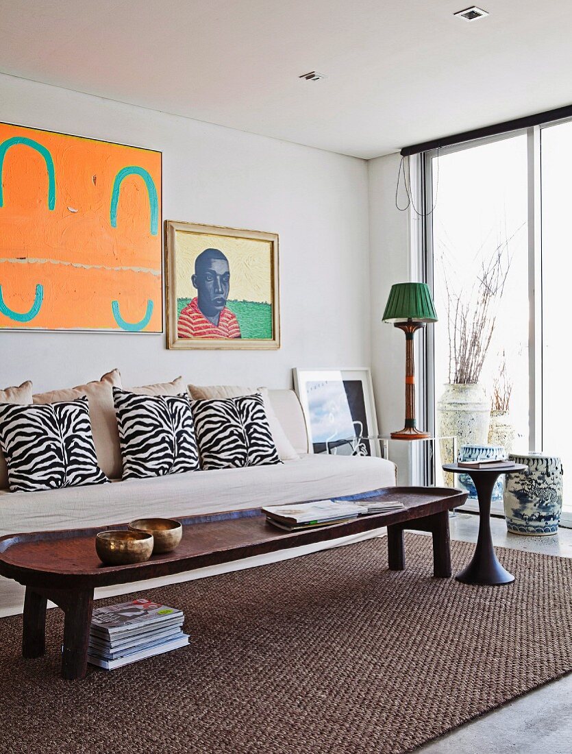 Rustikaler Holz Couchtisch auf Sisalteppich vor heller Couch mit Kissen im Zebra-Look und Bilder an Wand