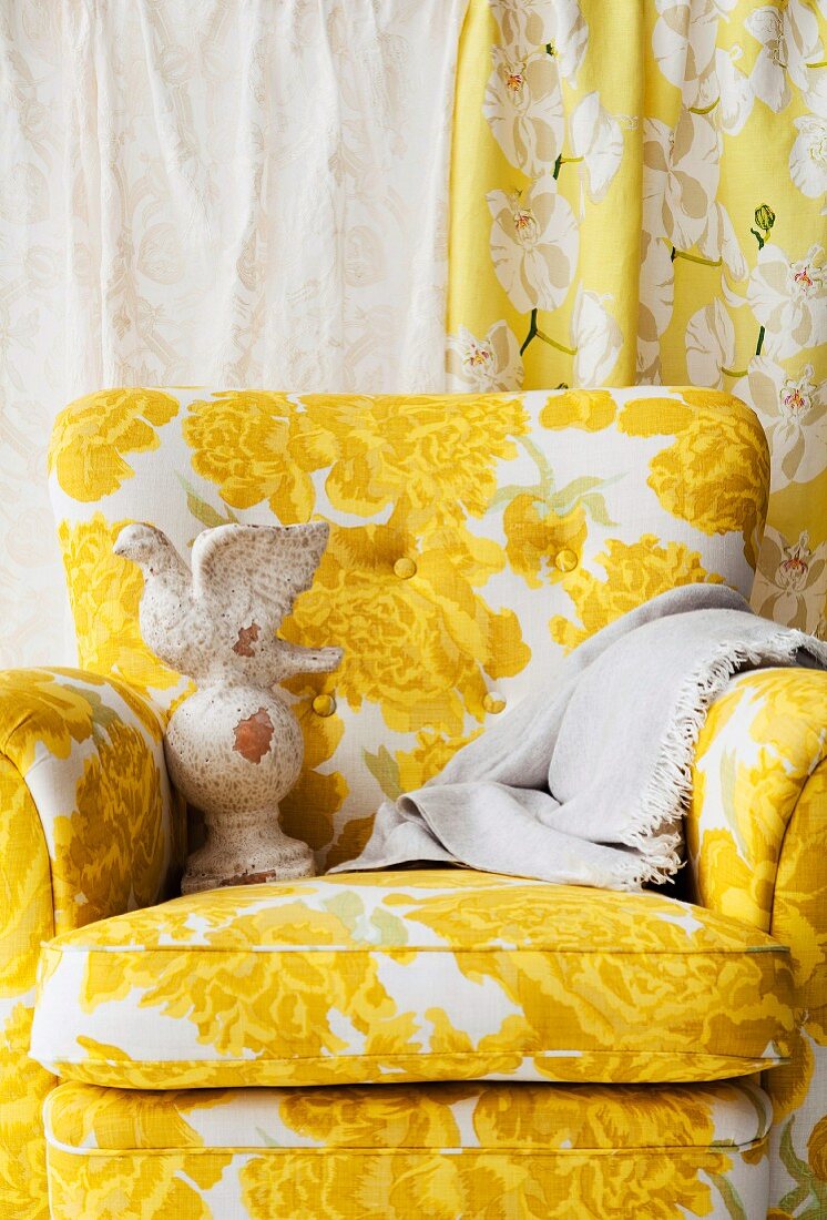 Armchair with yellow and white floral cover and vintage sculpture of bird