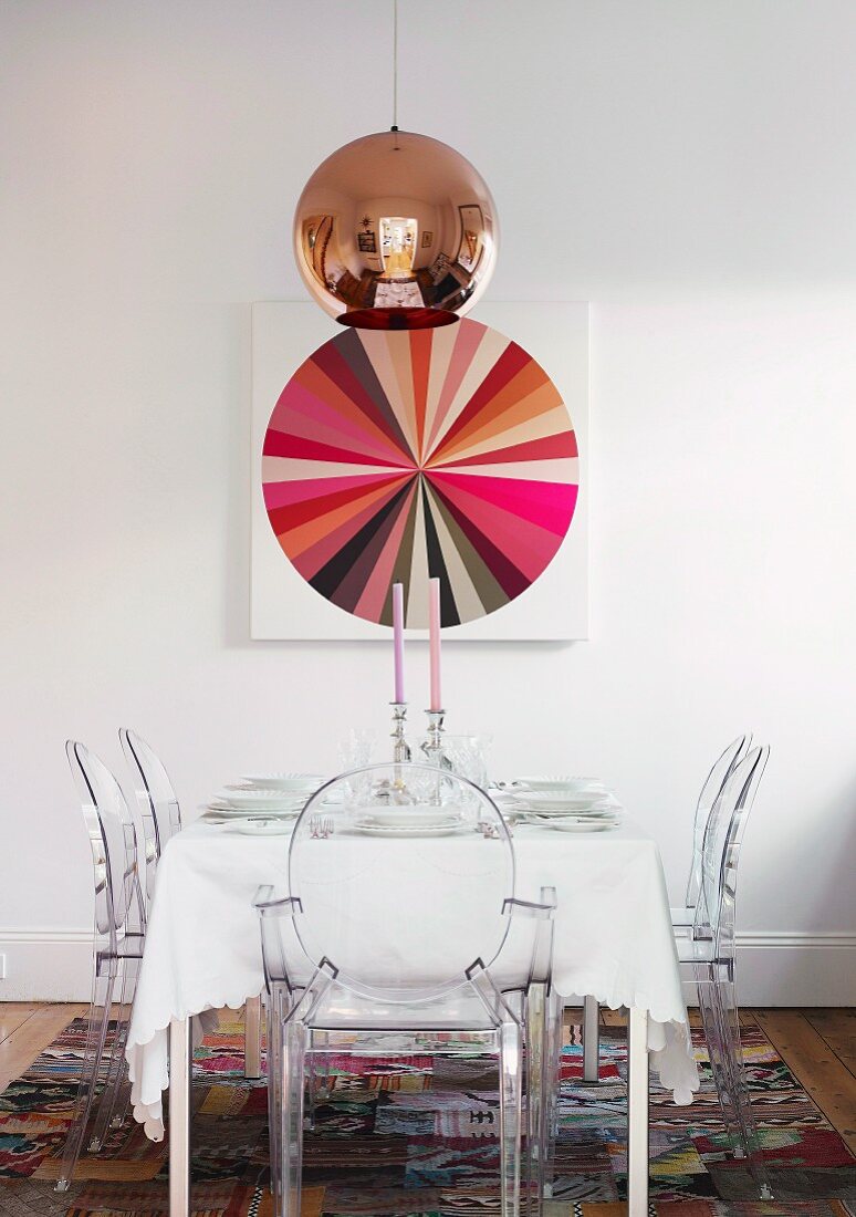 Kupfer Pendelleuchte über festlich gedecktem Tisch mit Ghost Stühlen und Farbkreis-Bild an der Wand