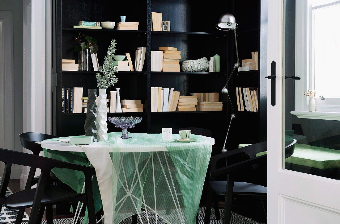 View through open door of table with transparent tablecloth and black chairs in front of black fitted shelving