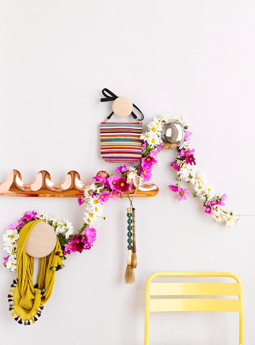 Coat pegs decorated with wreath of flowers on wall above backrest of yellow chair