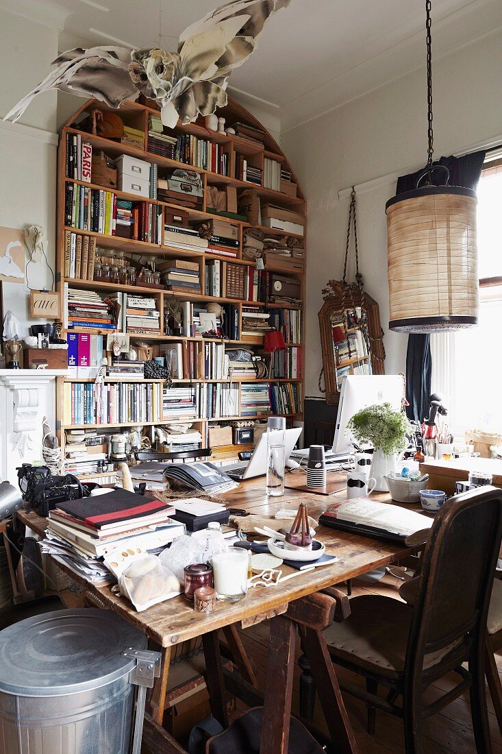 Crammed office with large, overloaded desk and bookcase in background