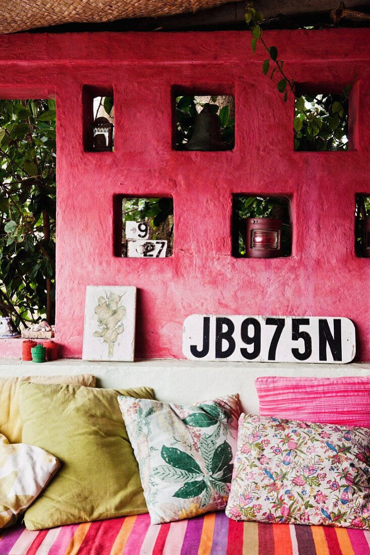 Gemauertes Sofa mit Kissen vor pinkfarbener Aussenwand mit Deko-Nischen und Autokennzeichen