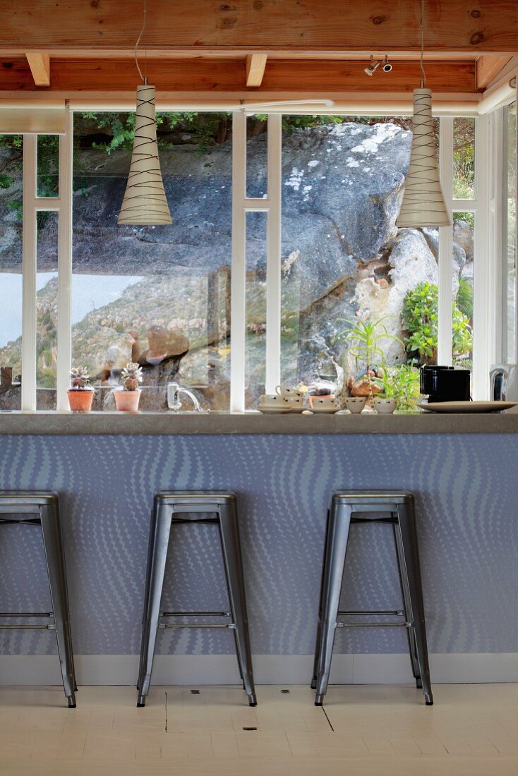 Metall Barhocker mit Retro Touch vor Theke und Blick durch Fenster auf Felswand