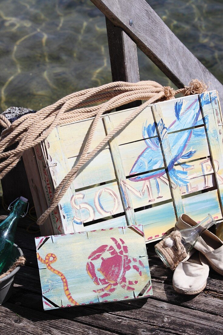 Mit Acrylfarbe sommerlich maritim bemalte, alte Obstkisten auf Holzsteg am Seeufer