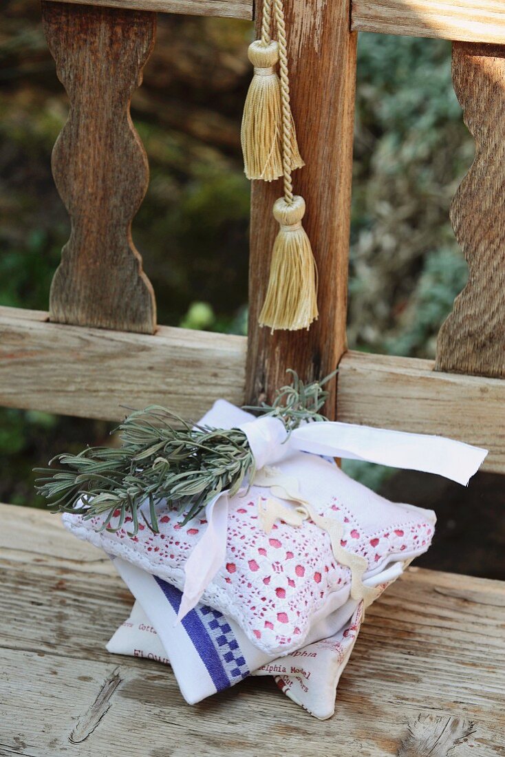 Aus Servietten, Tischtüchern und alten Spitzendecken selbstgenähte Duftkissen, mit Lavendelzweig zusammengebunden auf einer Holzbank