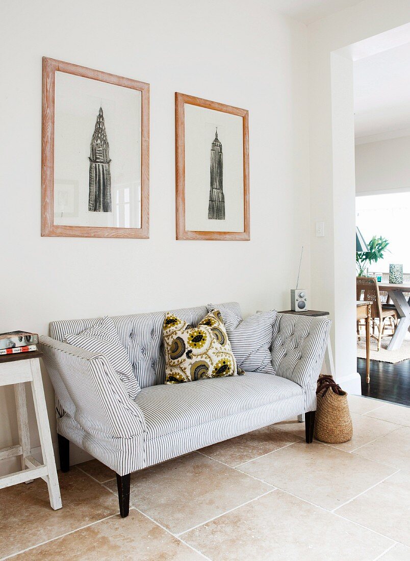 Framed drawings above two-seater sofa with pattern of narrow stripes in tiled hallway