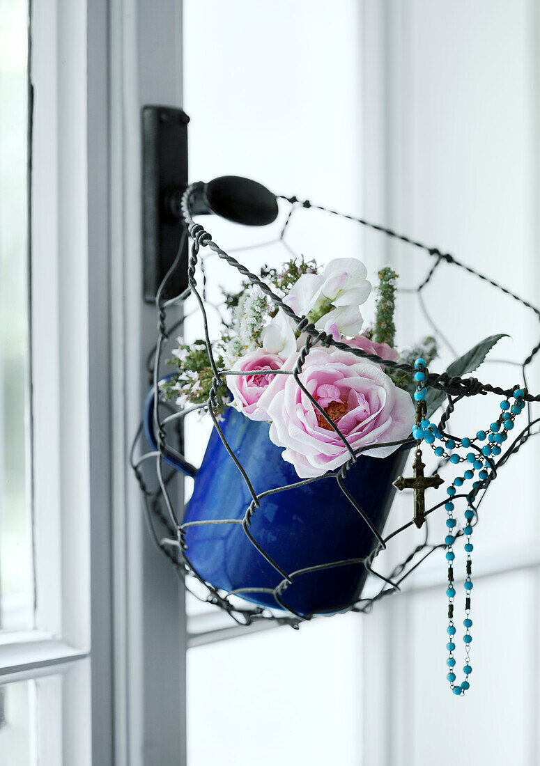 Hängender blauer Topf mit Rosen und Rosenkranz am Fenster