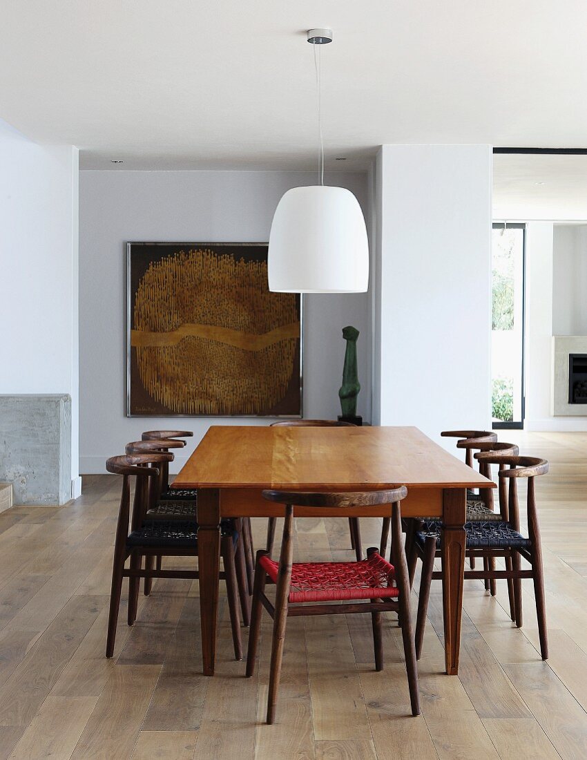 Simply wooden table and Scandinavian-style chairs below white pendant lamp in open-plan interior