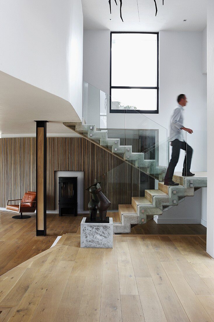 Offener Treppenraum mit Skulptur auf Podest vor Treppenaufgang und Mann in zeitgenössischem Wohnhaus