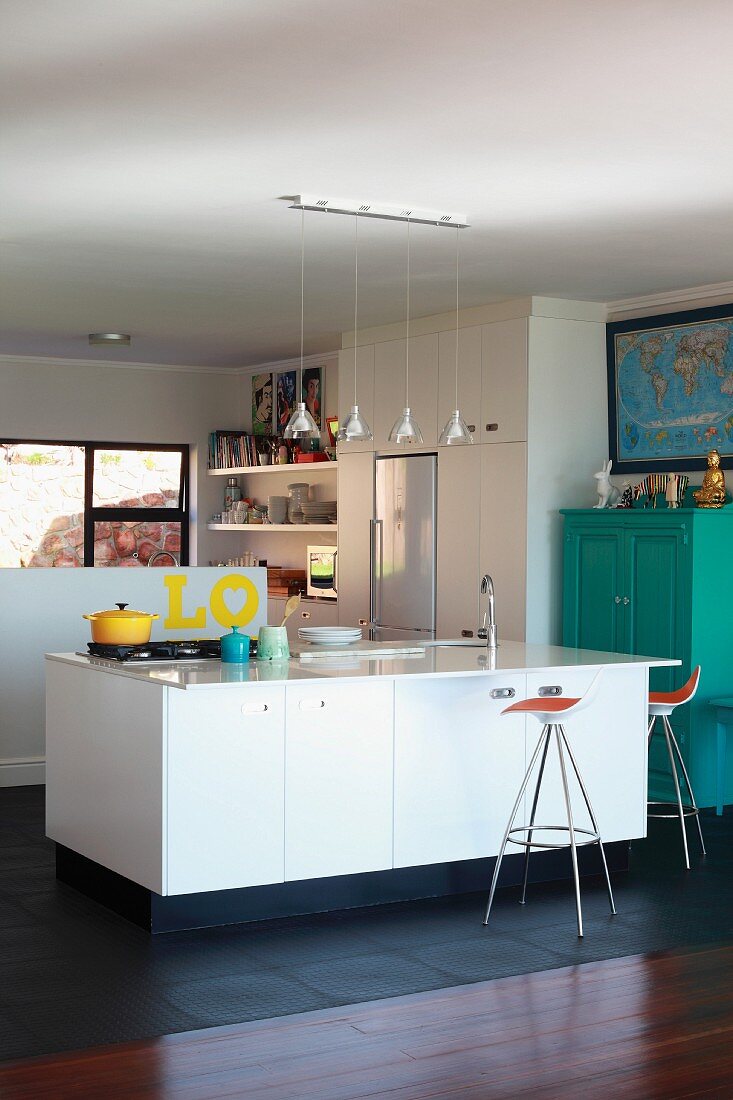 Reihe mit Pendelleuchten über Kücheninsel mit Spüle und Barhockern; türkisfarbener Schrank an einer Seite der offenen Küche