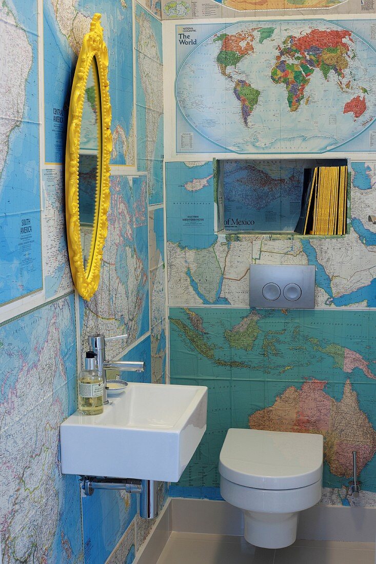 Mit Landkarten beklebte Wände in Gäste-WC mit goldgerahmtem Ovalspiegel über modernem Waschbecken