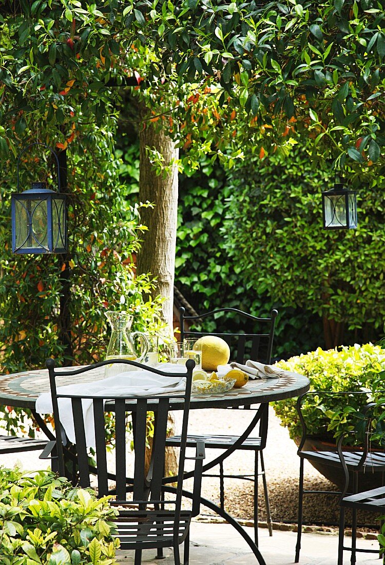 Refreshing drinks on metal garden table with matching chairs and lanterns hanging from tree in sunny garden