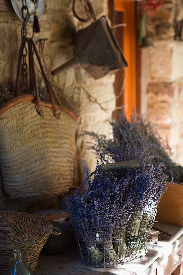 Getrocknete Lavendelsträusse im Drahtkorb vor an rustikaler Wand gehängte Einkaufstasche
