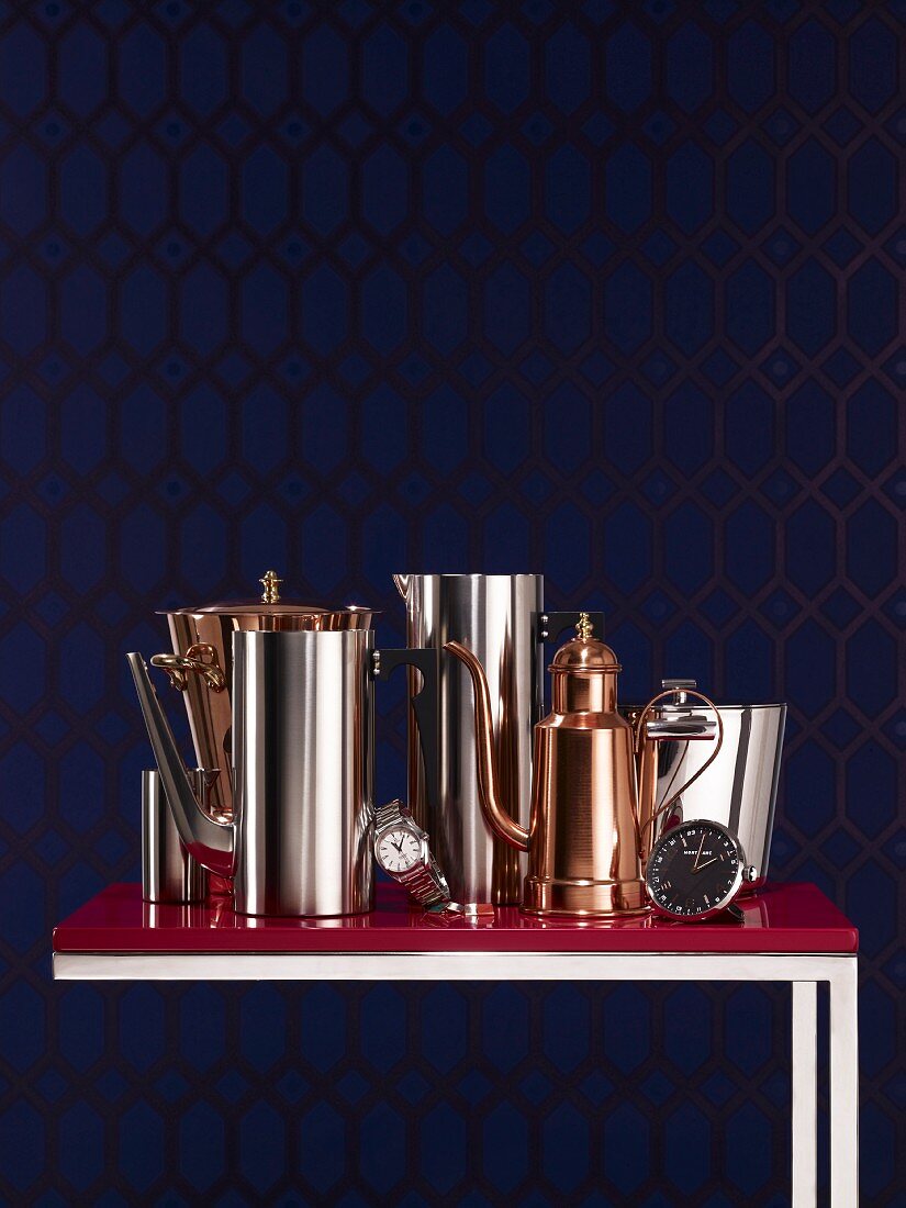 Pots and vessels made from traditional copper and modern stainless steel on Bordeaux red side table against midnight blue background