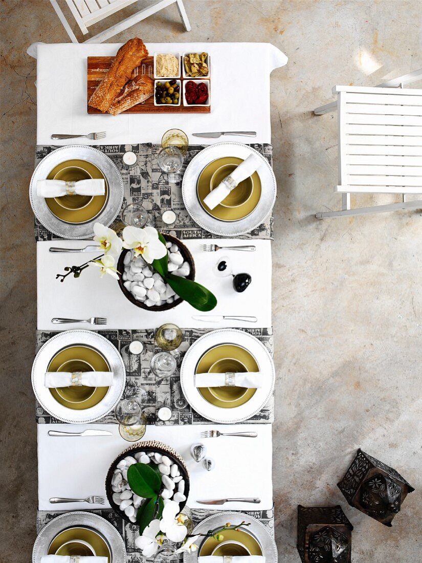 Blick von oben auf Gedecke mit weissen Stoffservietten und angerichteten Vorspeisen auf weisser Tischdecke mit Tischläufern