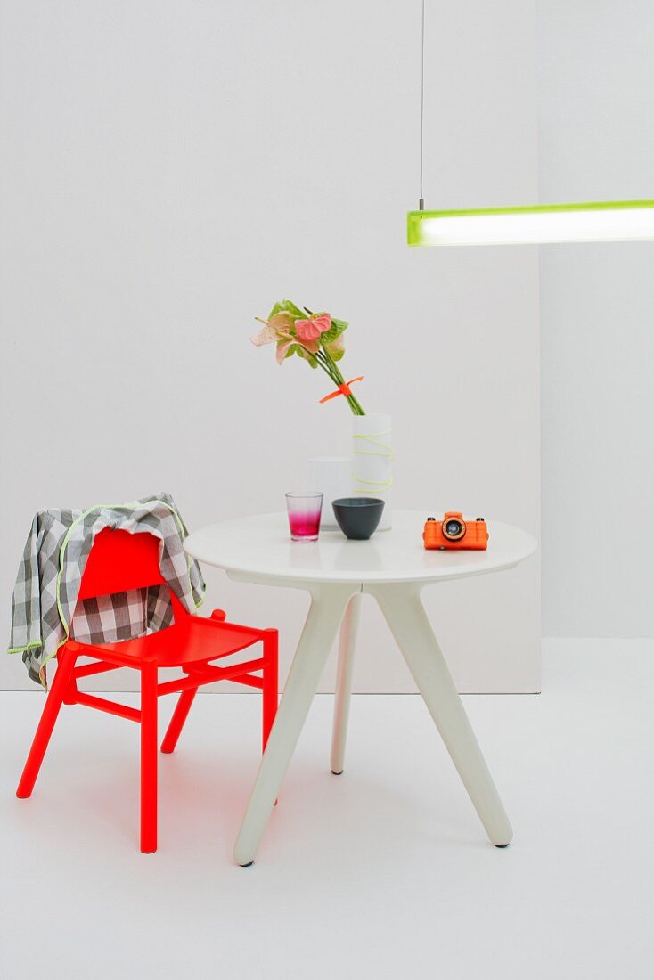 Modern dining set for one with bright red chair and small, three-legged table below purist strip light