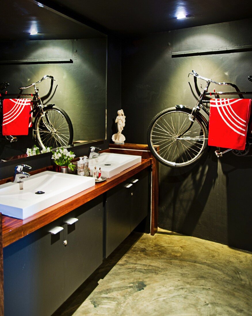 Dark-painted bathroom with modern washstand and bicycle hung on wall used as towel rack