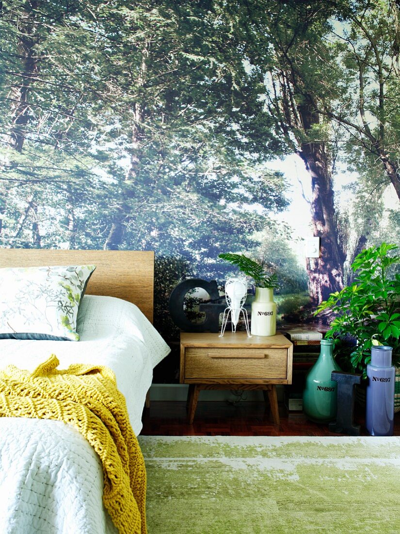 Fototapete mit Waldmotiv in Schlafzimmer; ergänzende Accessoires in Form von Pflanzendeko und Kopfkissen mit Floral-Druck