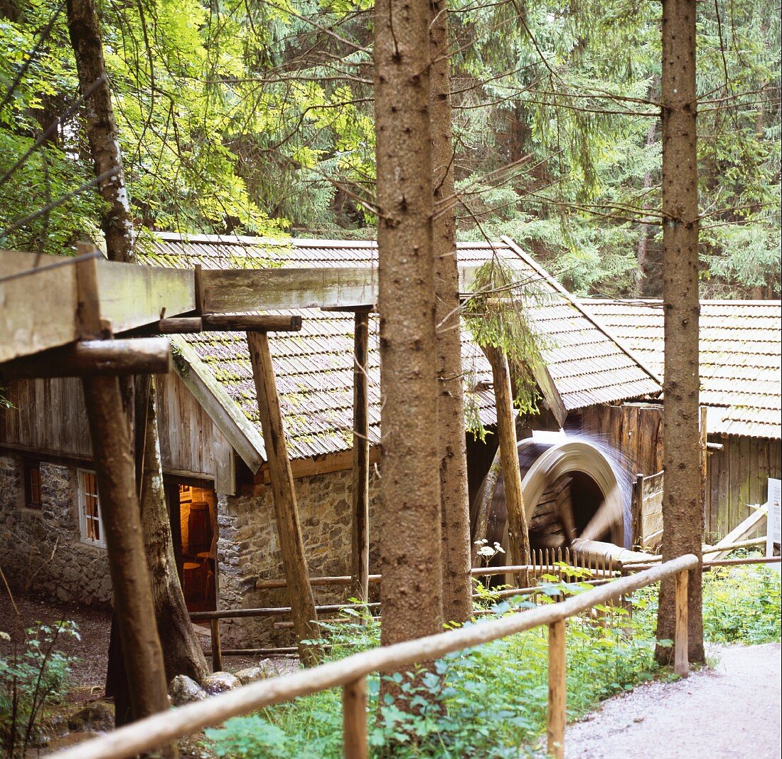 Historisches Mühlengebäude im Wald mit rotierendem Wasserrad, wirkt märchenhaft und versteckt