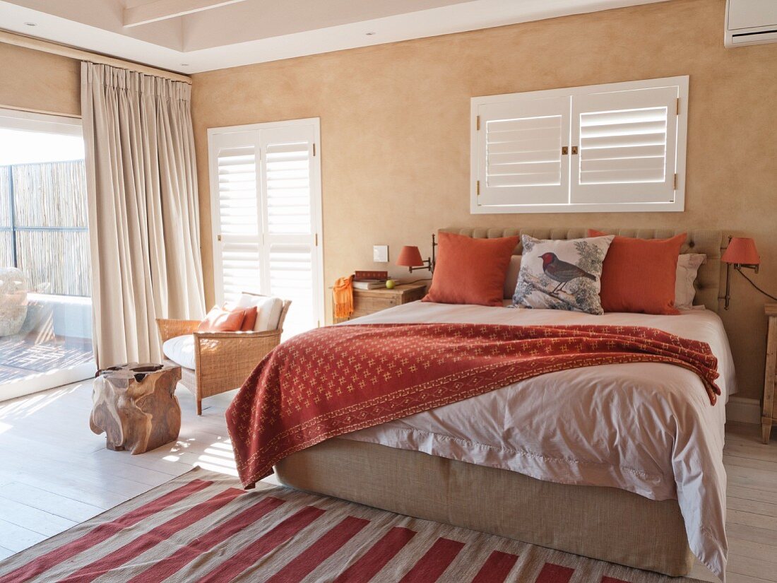 Mediterranean bedroom with double bed below window with closed interior shutters and floor-length curtains on terrace doors