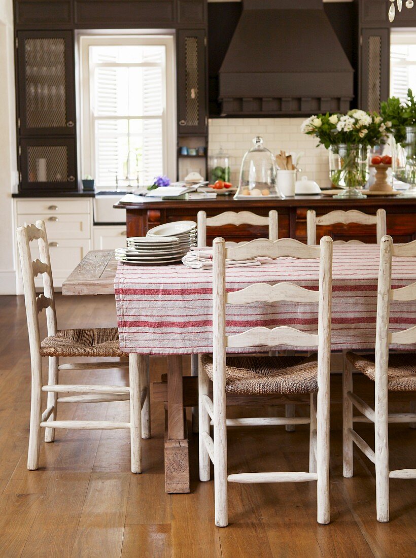 Rustikaler Tisch mit Tischdecke und Holzstühle mit Bast Sitzfläche in ländlicher Küche