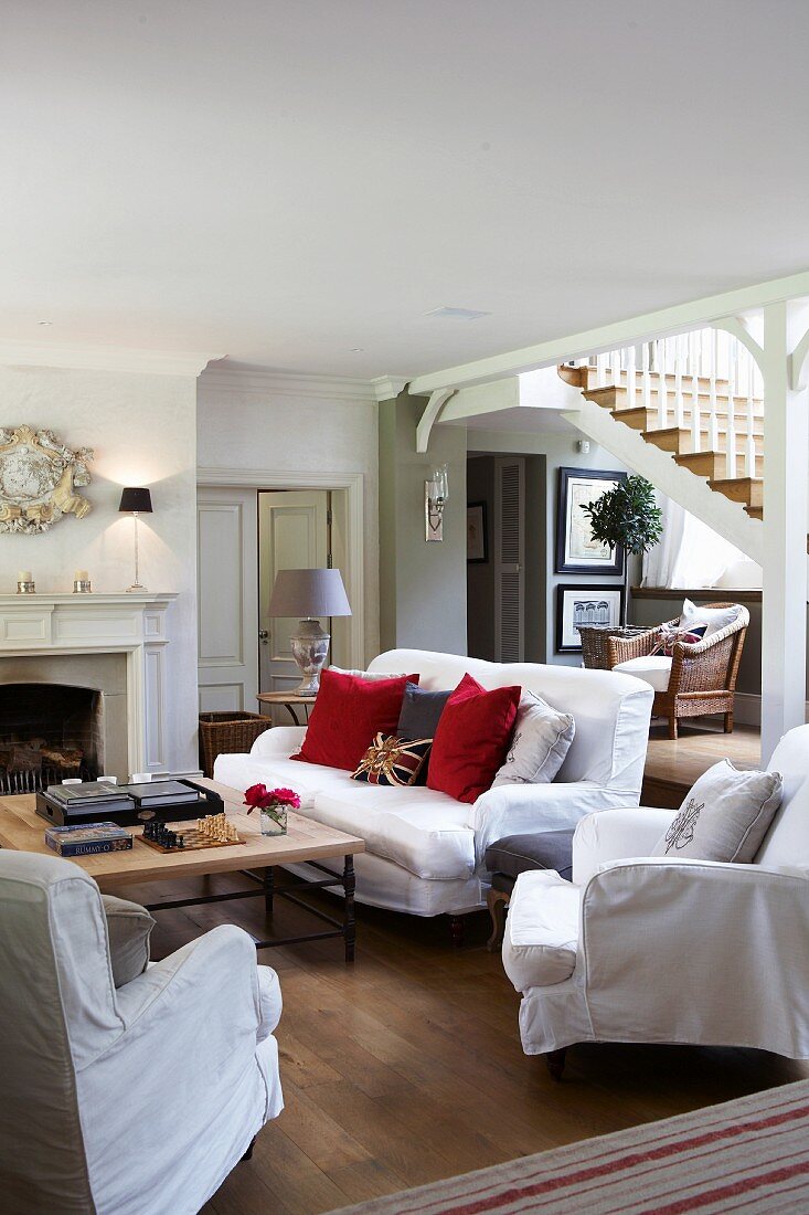Sofa set with white loose covers and coffee table in traditional country-house living room; open staircase in background