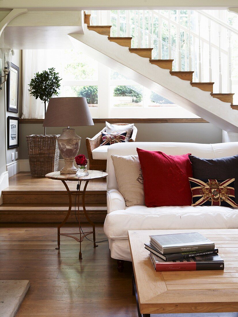 Sofa mit Kissen und Couchtisch vor Podest mit Stufen unter Treppenlauf in elegantem Landhaus