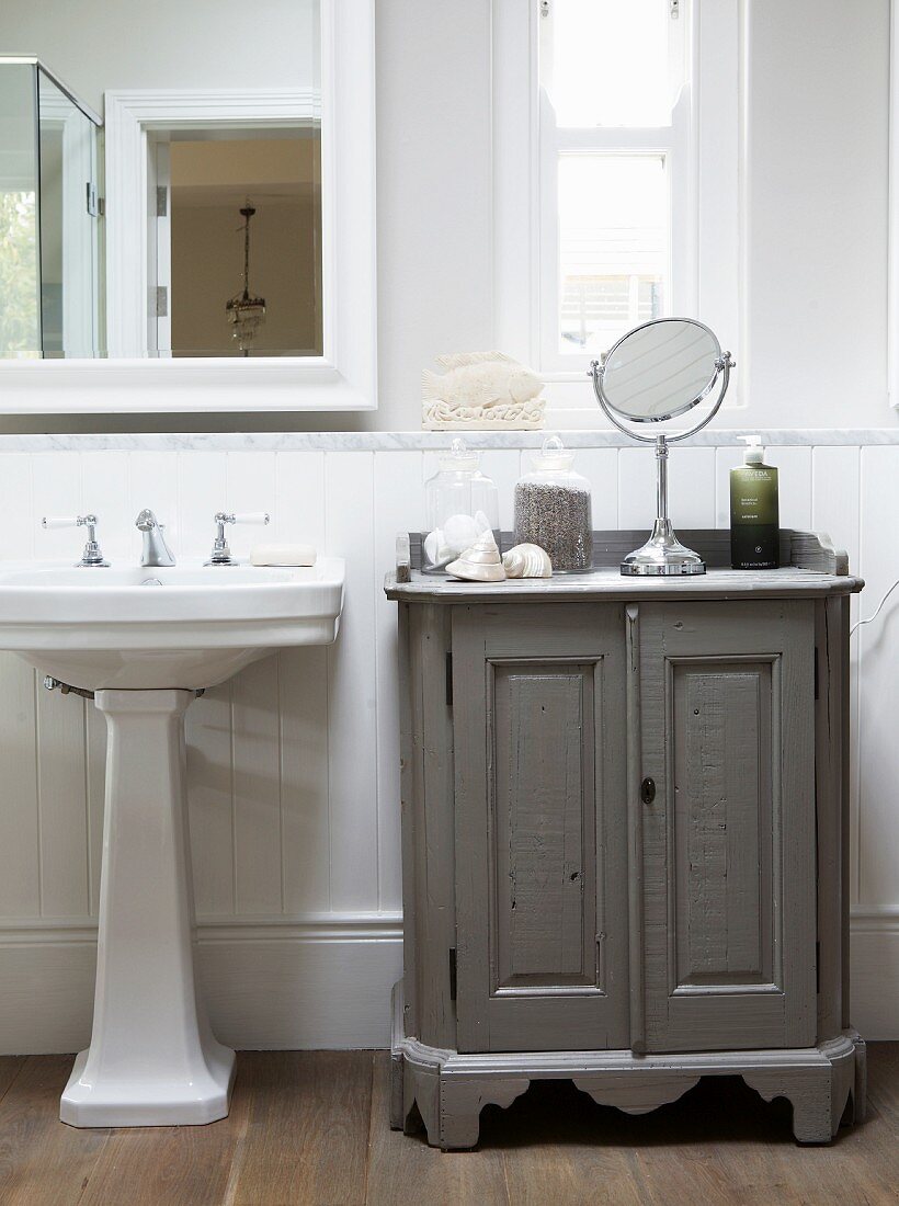 Pedestal washbasin and toiletries on vintage-style, half-height cabinet in traditional bathroom