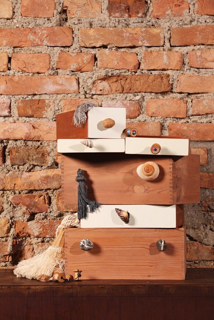 Gestapelte Kisten mit angeschraubten Möbelgriffen vor rustikaler Ziegelwand