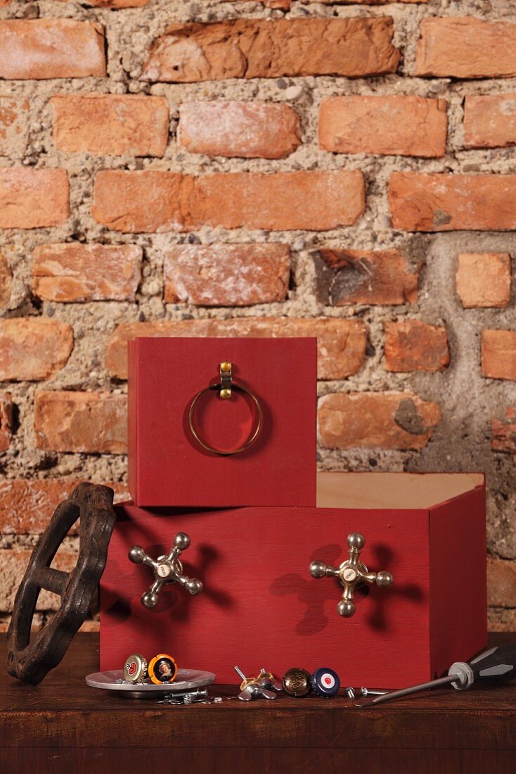 Gestapelte Kisten mit rotbraunen Fronten und angeschraubten Bauteilen vor rustikaler Ziegelwand
