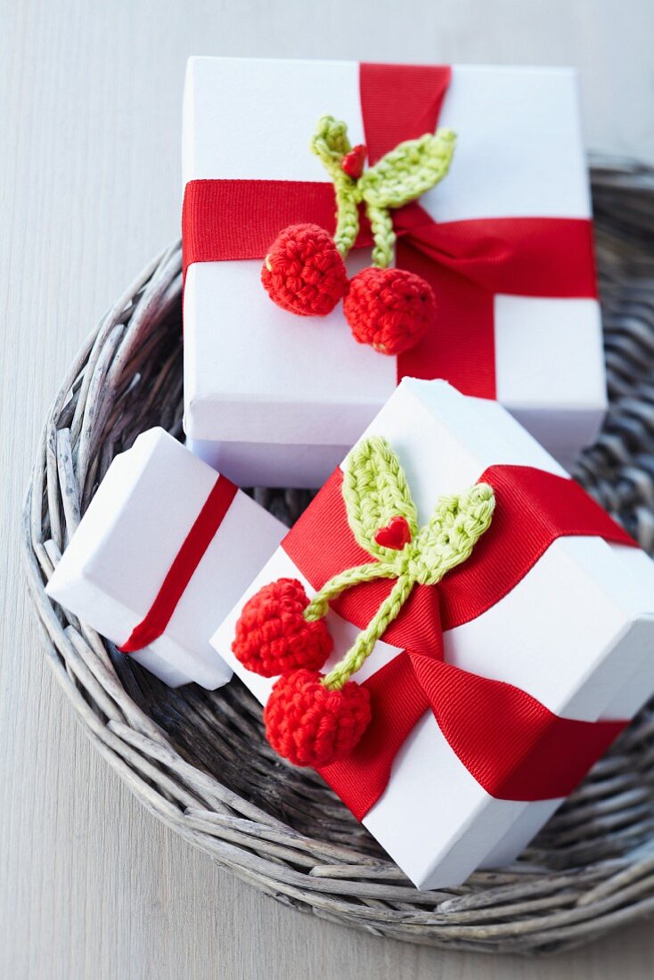Kleine Geschenkkartons verziert mit rotem Schleifenband und gehäkelten Kirschen