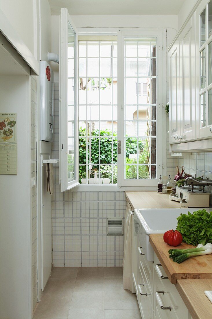 Vegetables on kitchen counter in narrow kitchen with open, barred window at far end