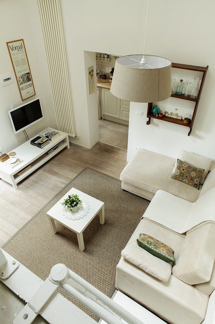 View down into lounge area with pale upholstered furniture on rug and wooden floor in modern setting