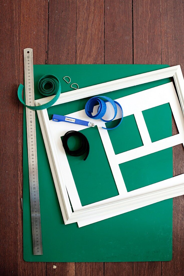 Grüner Fotokarton mit weißem Bilderrahmen und Passepartout, dazu Metalllineal und Klettbänder auf Holzunterlage