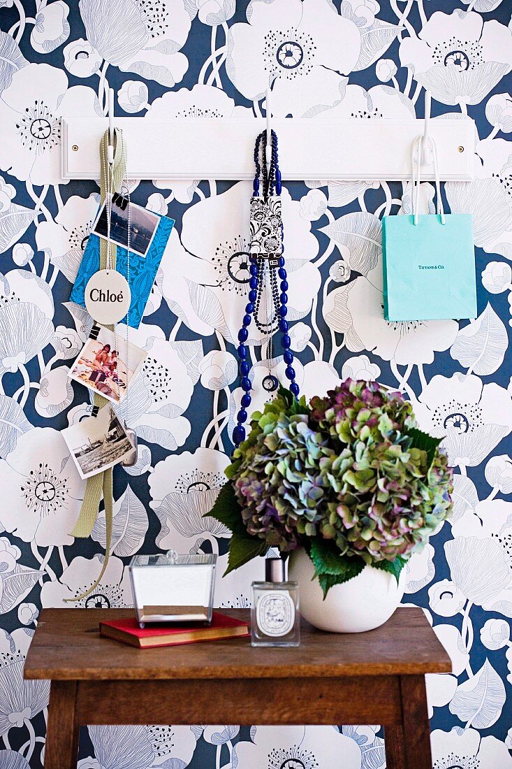 White wardrobe on wall with blue and white floral motif; in front of it dried hydrangea flowers in a balloon vase standing on a vintage table