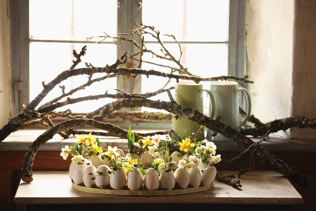 Gänseeier mit Frühlingsblumen dekoriert unter Ästen auf Wandtisch am Fenster