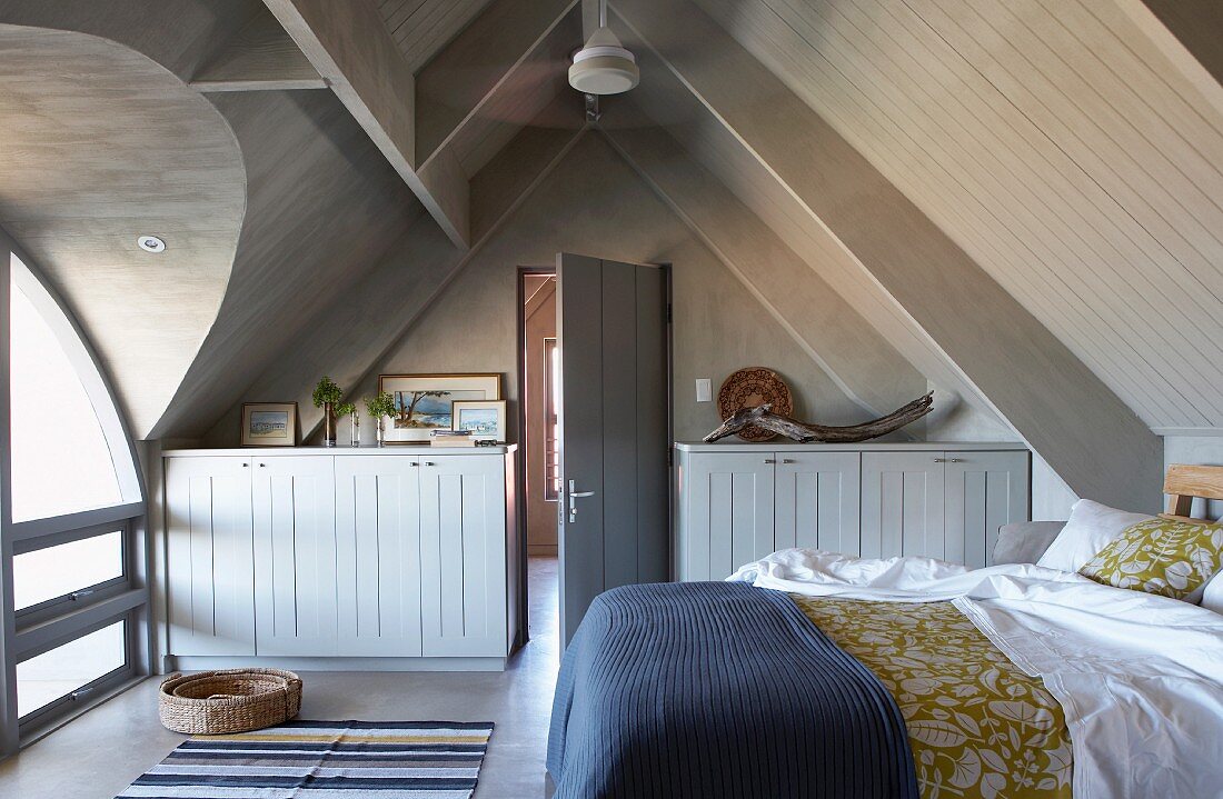 Schlafzimmer mit Doppelbett und Sideboards unter offenem Spitzdach mit Belichtung durch Tonnengaube