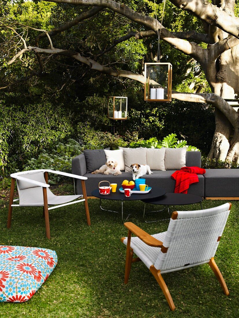 Sitzecke im Garten mit Sofa, Tischen, Stühlen, Laternen und Bodenkissen