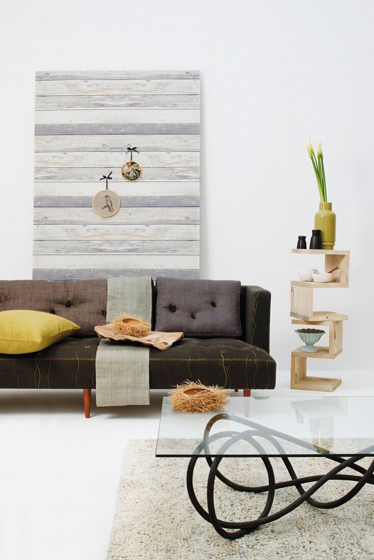 Sofa, Glastisch und additives Beistellregal mit Naturdeko vor Bretterwand in Grautönen