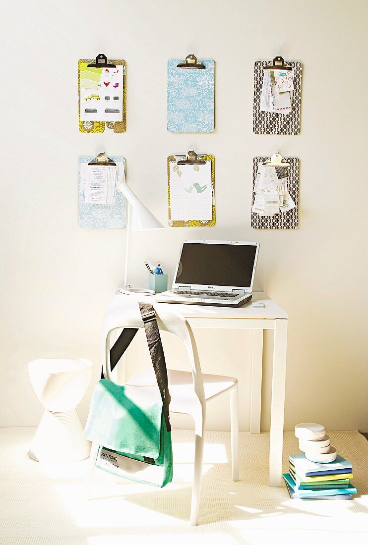 Selbstgestaltene Klemmbretter an der Wand, davor kleiner weißer Arbeitstisch mit Laptop und weißem Stuhl