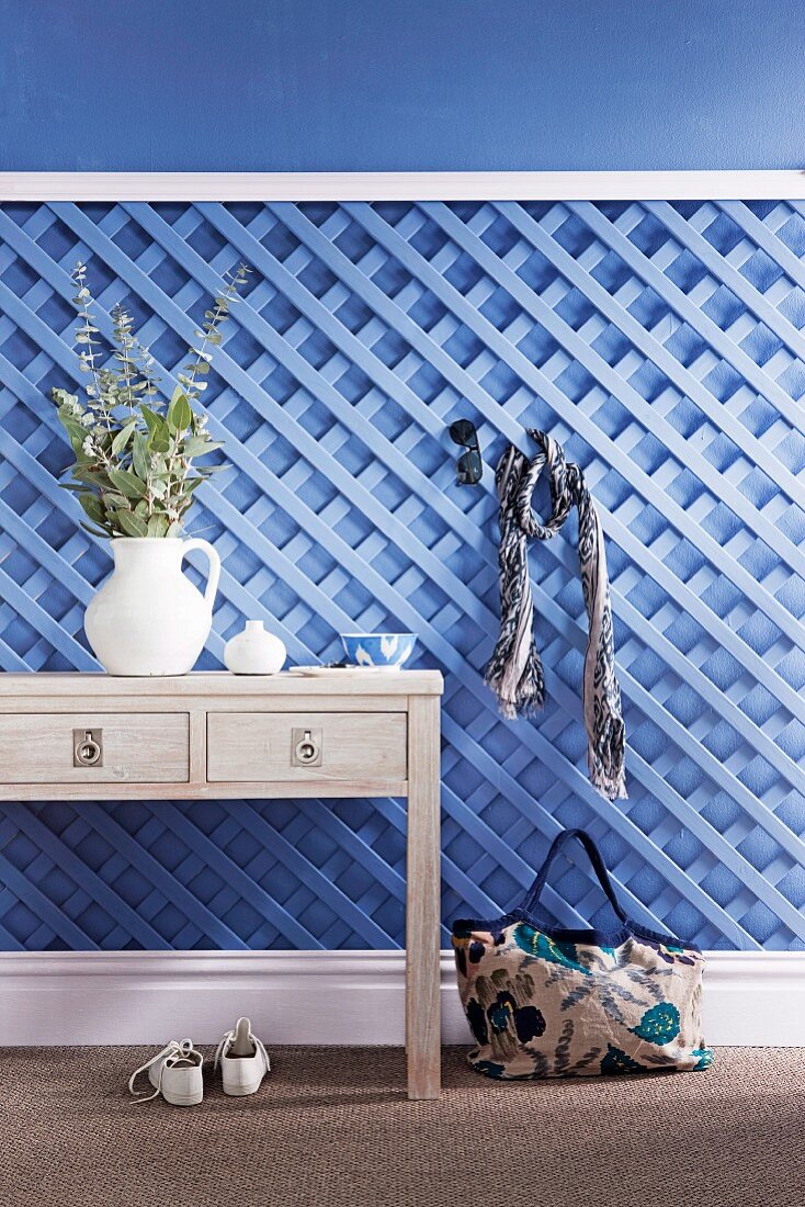Holzspalier hellblau gestrichen als Garderobe nutzbar, davor ein Schubladentisch mit Dekoration