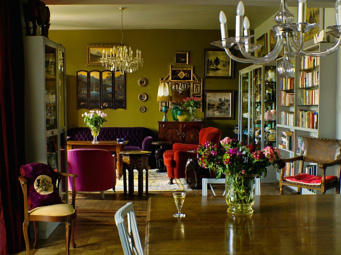 View across dining table below chandelier into atmospheric living area with armchairs in various colours