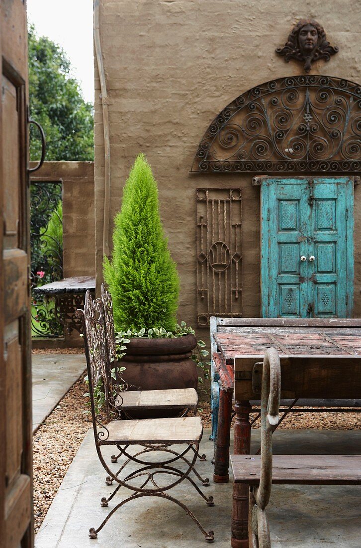Französische Drahtstühle, ein Klostertisch und kunstvolle, fligrane indische Eisenfenster in einem mit großen Betonplatten und Kiesstreifen gestalteten Innenhof