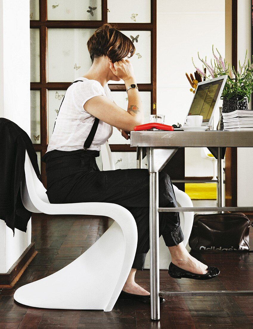 Woman sitting on white Panton chair working on laptop