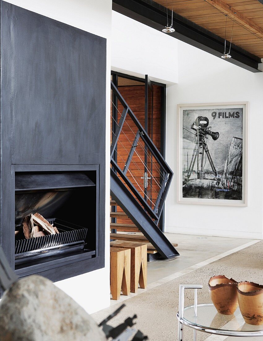 Open fireplace with metal surround in living room; staircase in background